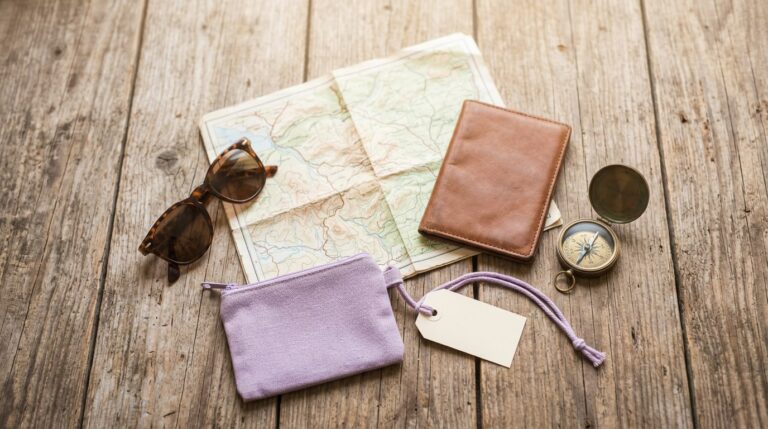 Travel quotes for vision board: a folded map, compass, sunglasses and a blank luggage tag on wood